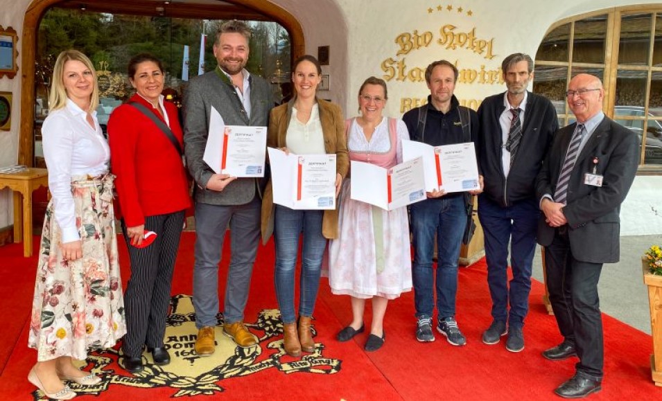 8 Leute die vor einem Hotel stehen und Zertifikate heben.