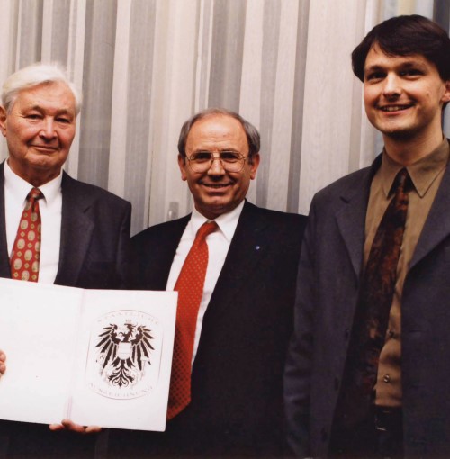 Drei Männer mit einer weißen Mappe in der Hand.