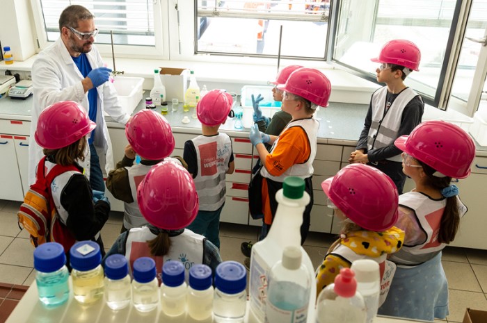Eine Gruppe von Kindern mit Schutzhelmen in einem Labor.