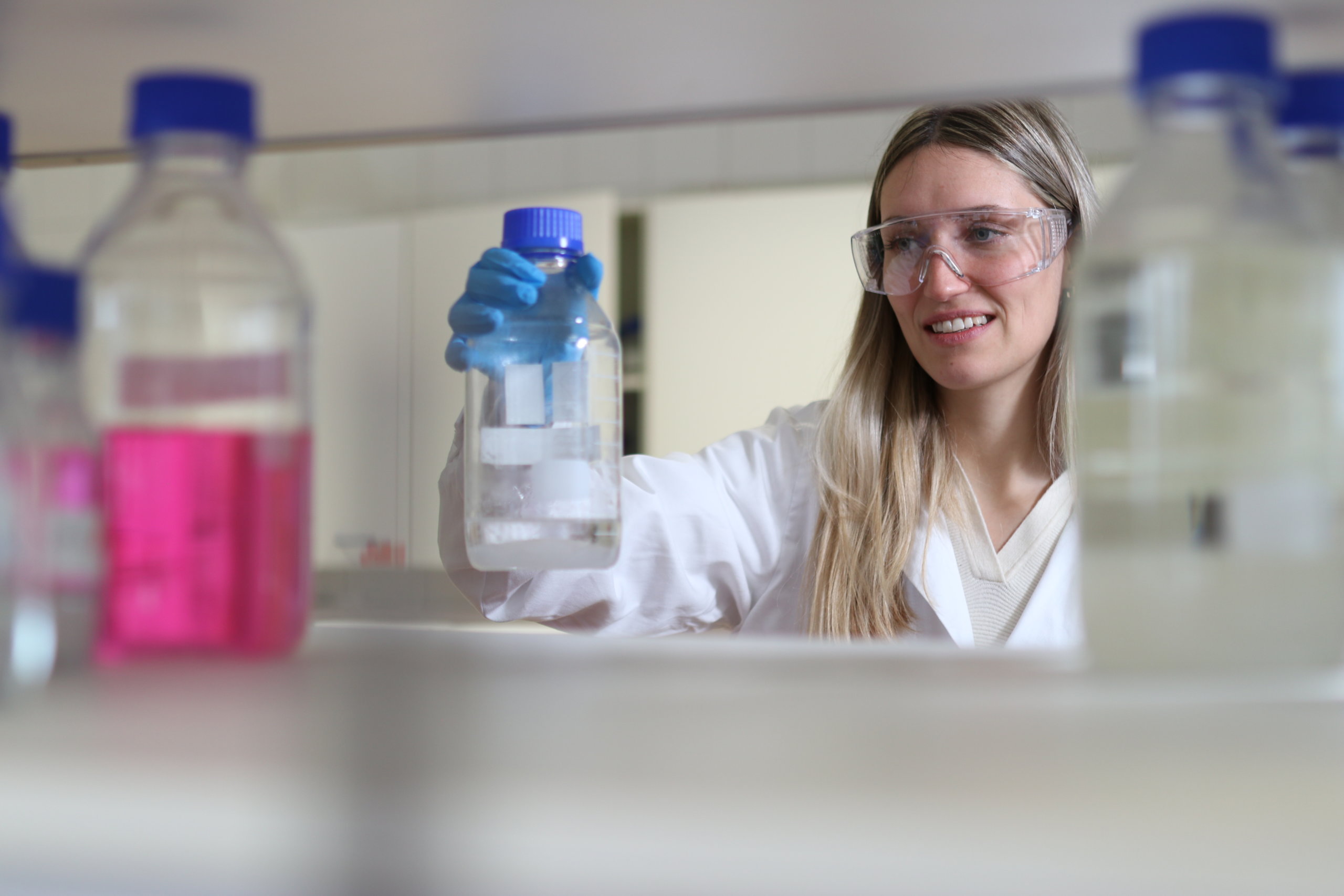 Eine Frau im Laborkittel hält eine Flasche Flüssigkeit in der Hand.