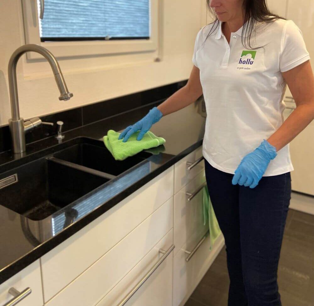 Frau putzt mit grünem Mikrofasertuch die Arbeitsfläche in der Küche,