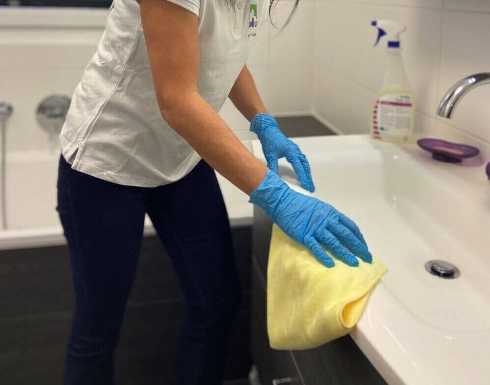 Frau putzt mit gelbem Mikrofasertuch das Waschbecken im Bad.