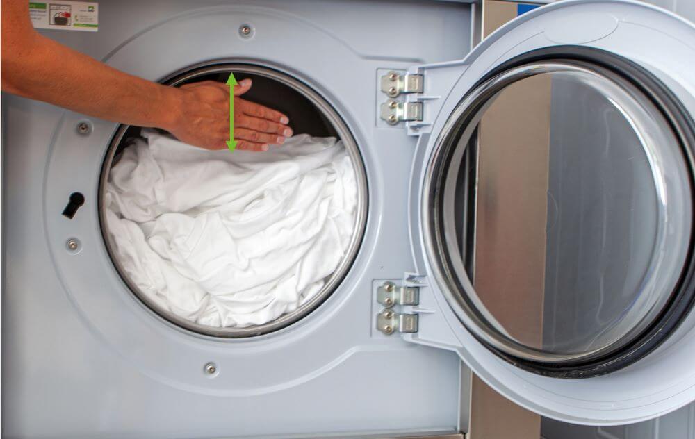 richtige Waschmaschinenbeladung, gefüllte Waschmaschine mit vorgehaltener Hand demonstriert richtige Washcmaschinenbeladung mit 1 Handbreite / 10 cm Freiraum zum oberen Rand der Trommel